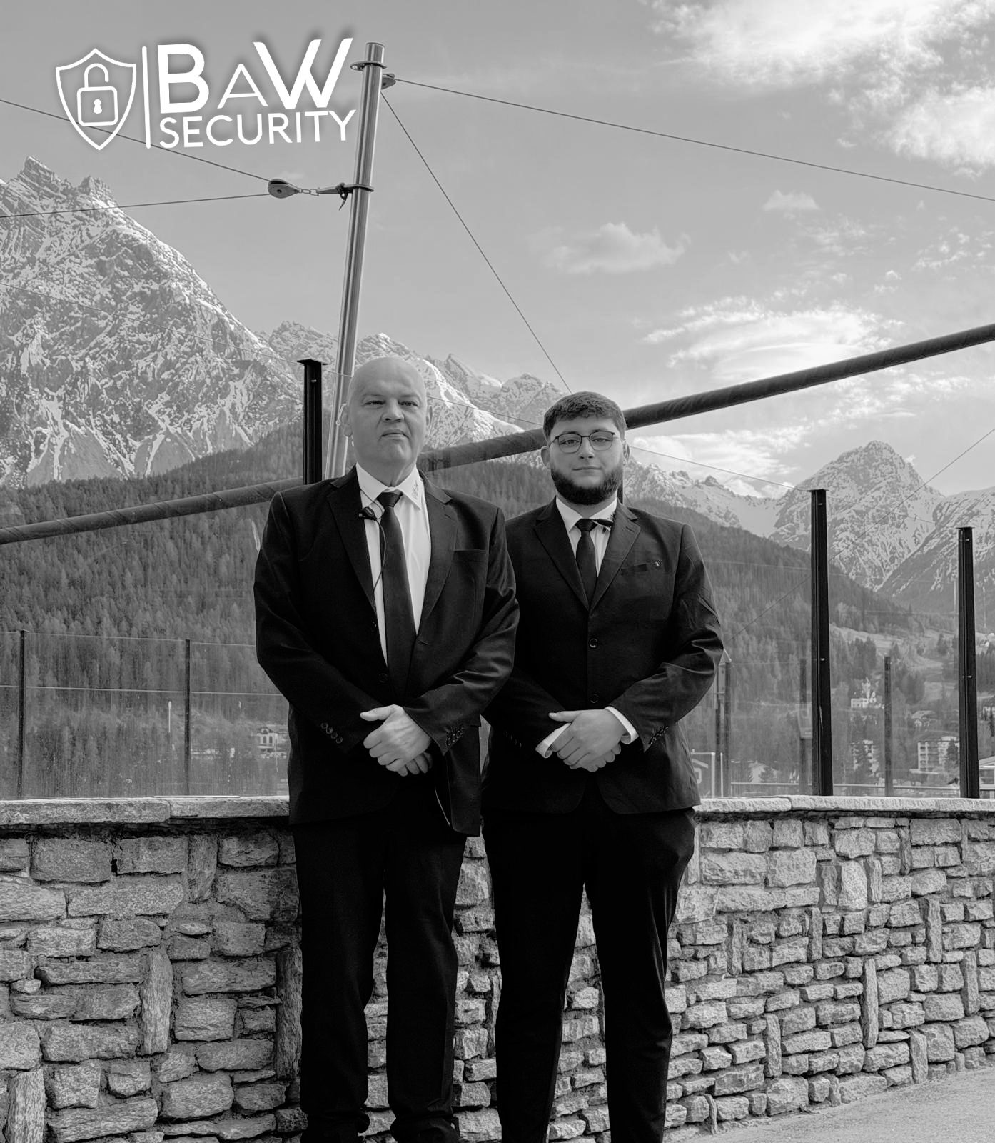 Zwei Personenschützer im Anzug vor Bergkulisse, schwarzweiss